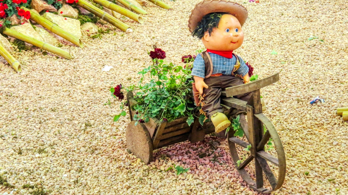 a doll sitting on top of a wooden wheelbarrow filled with plants