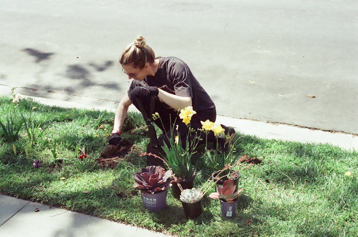 a woman kneeling down in the grass next to a potted plant