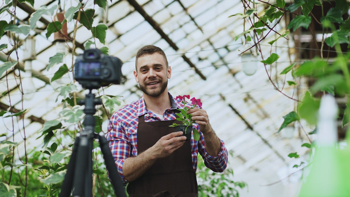 Man filming himself holding plants in a greenhouse.