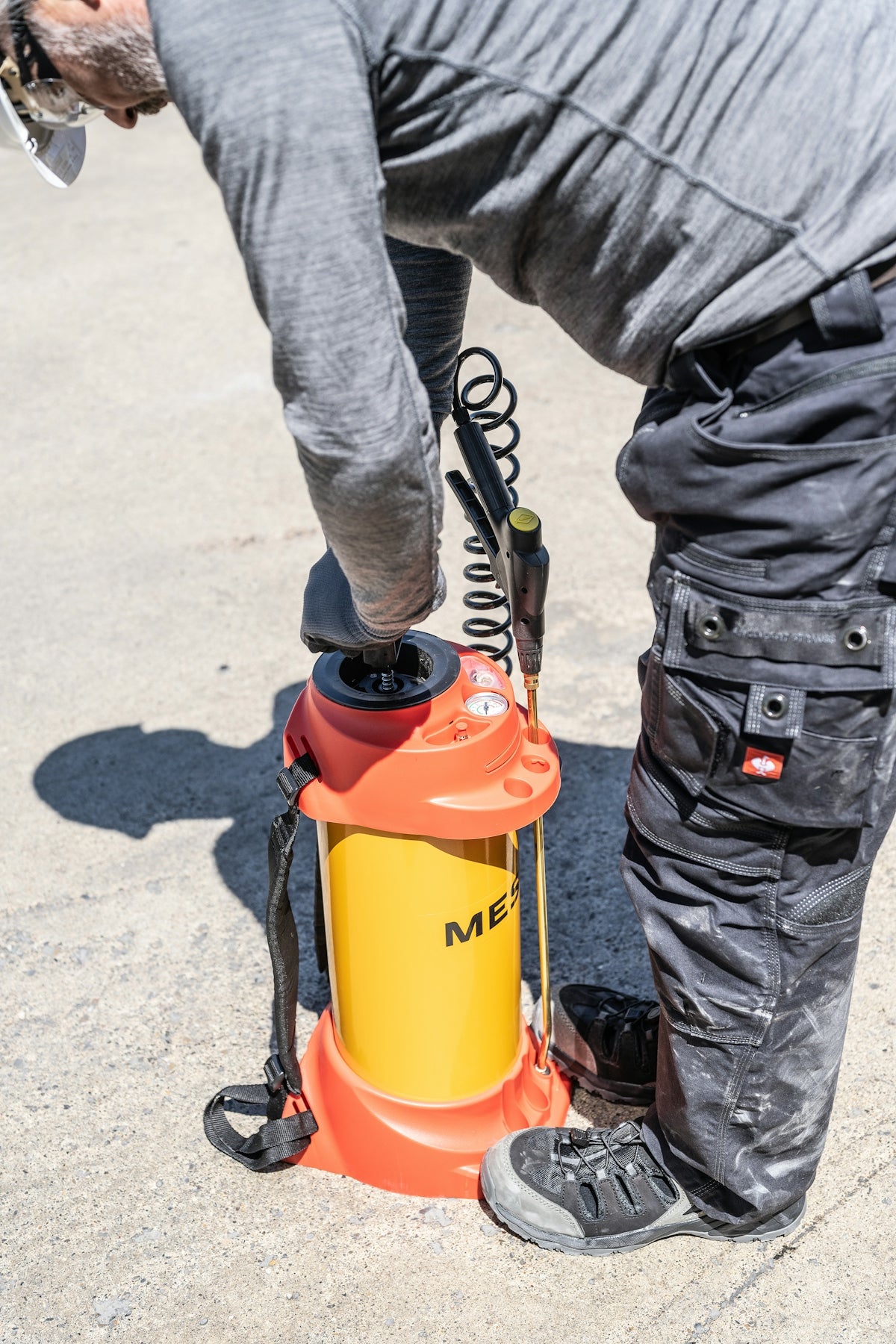 Man operating a yellow and orange pressure sprayer outdoors.