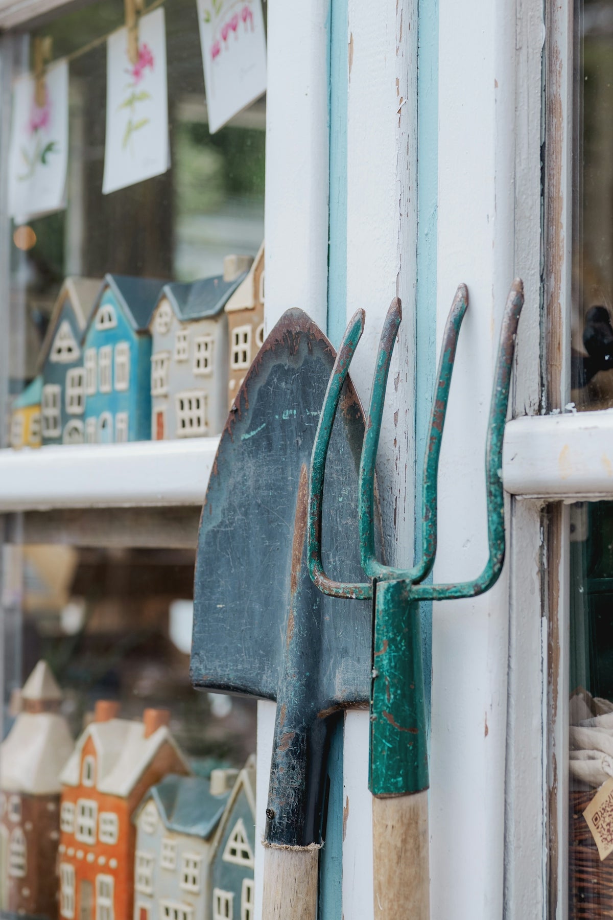 Rustic garden tools leaning against a window with decorative houses.