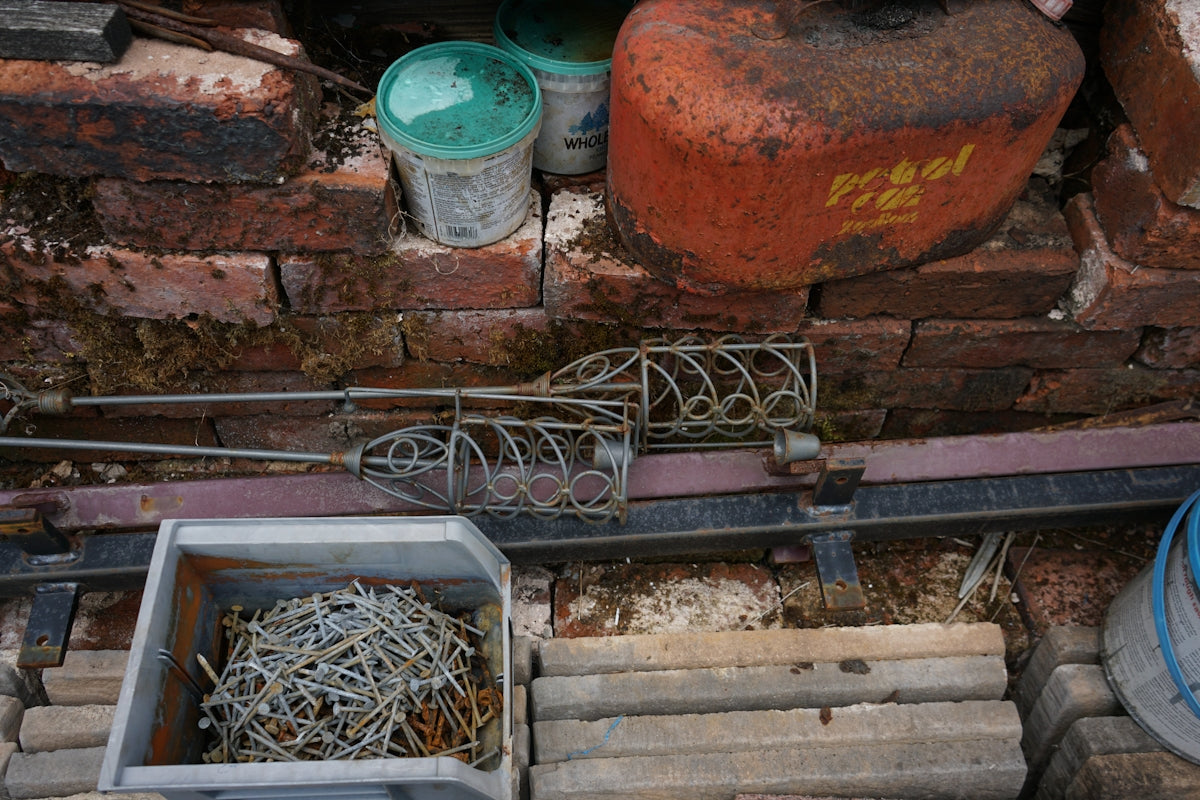 Rusty tools and discarded items against an old brick wall.