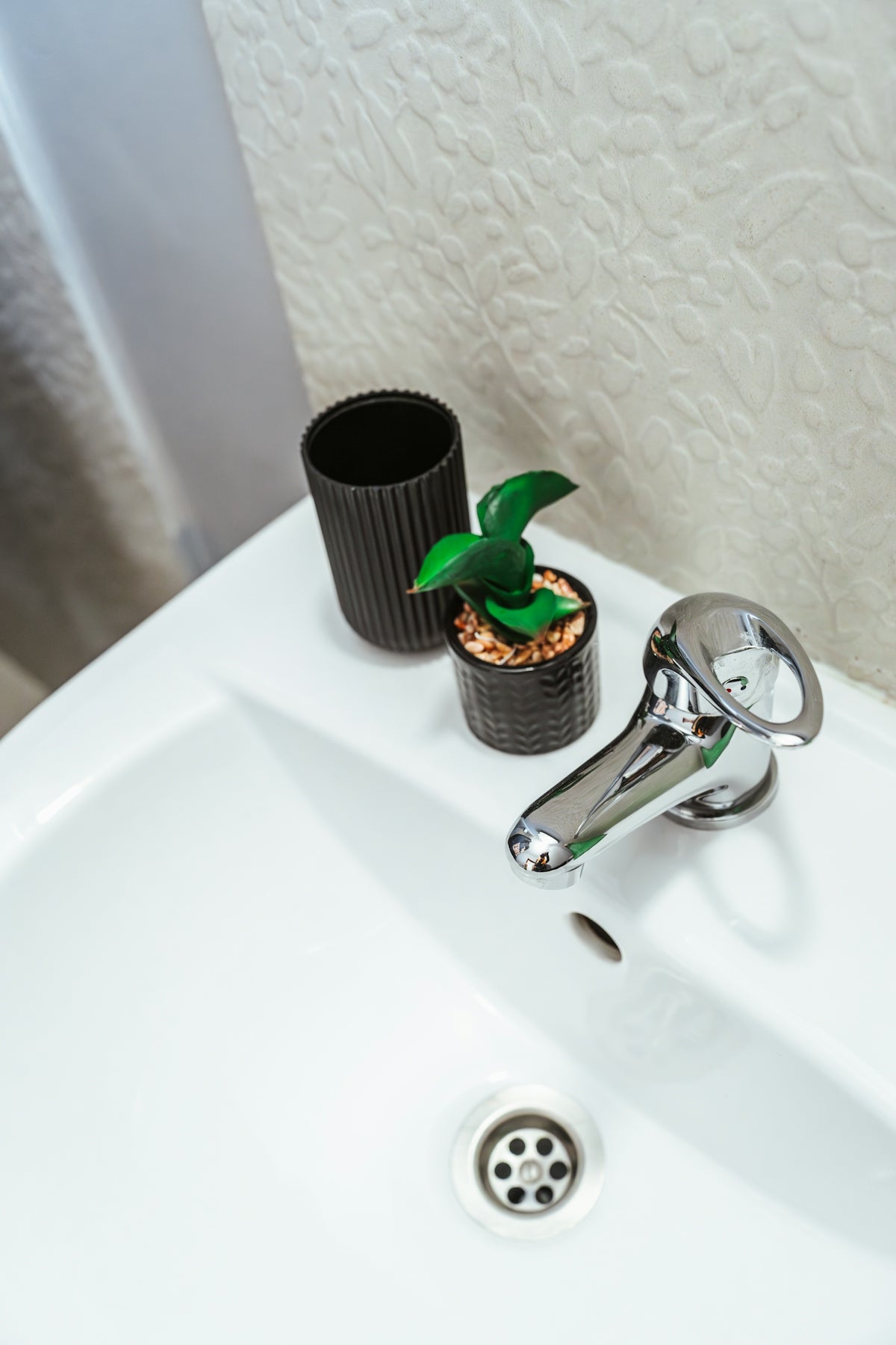 a bathroom sink with a green plant and a black cup