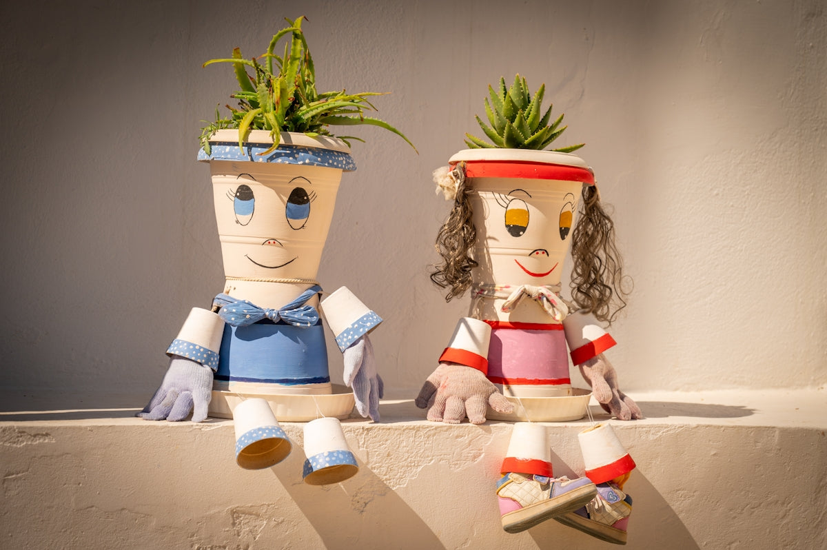 Two quirky plant pots shaped like people sitting together.