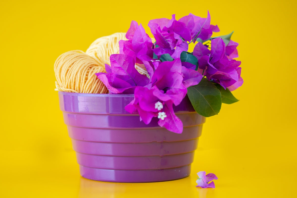 Purple pot with flowers and yarn against yellow background